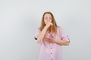 blonde haired woman suffering from cough in shirt and looking unwell. front view.